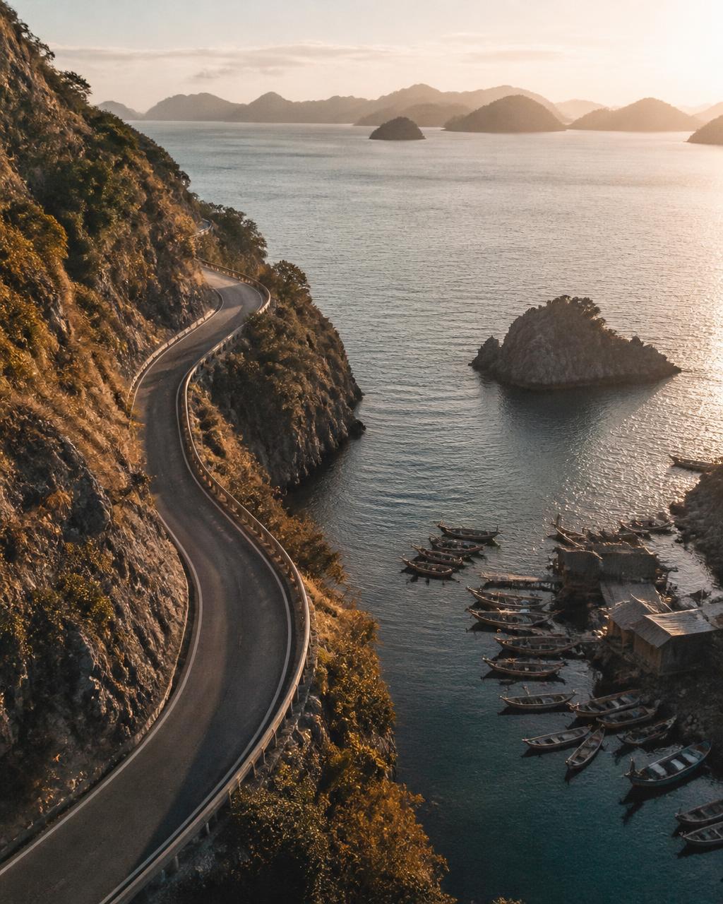 Winding coastal road above a harbour and distant islands at golden hour